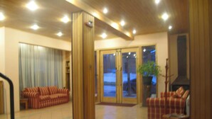 A spacious living room with a large sofa set, a fireplace, and a view of the outdoors through glass doors. - Hotel Saltos del Paine (Natales)