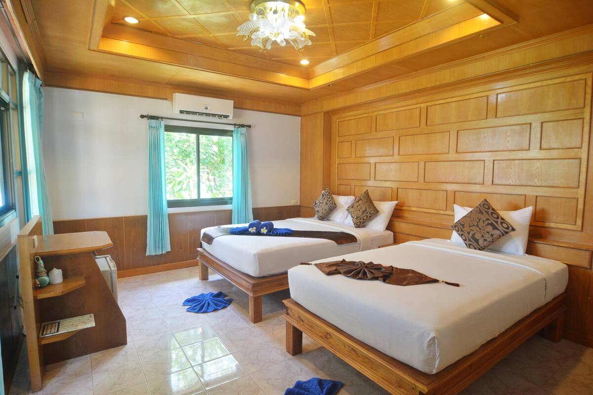 A hotel room with two beds, wooden headboard panels, a small desk, and a window with curtains.