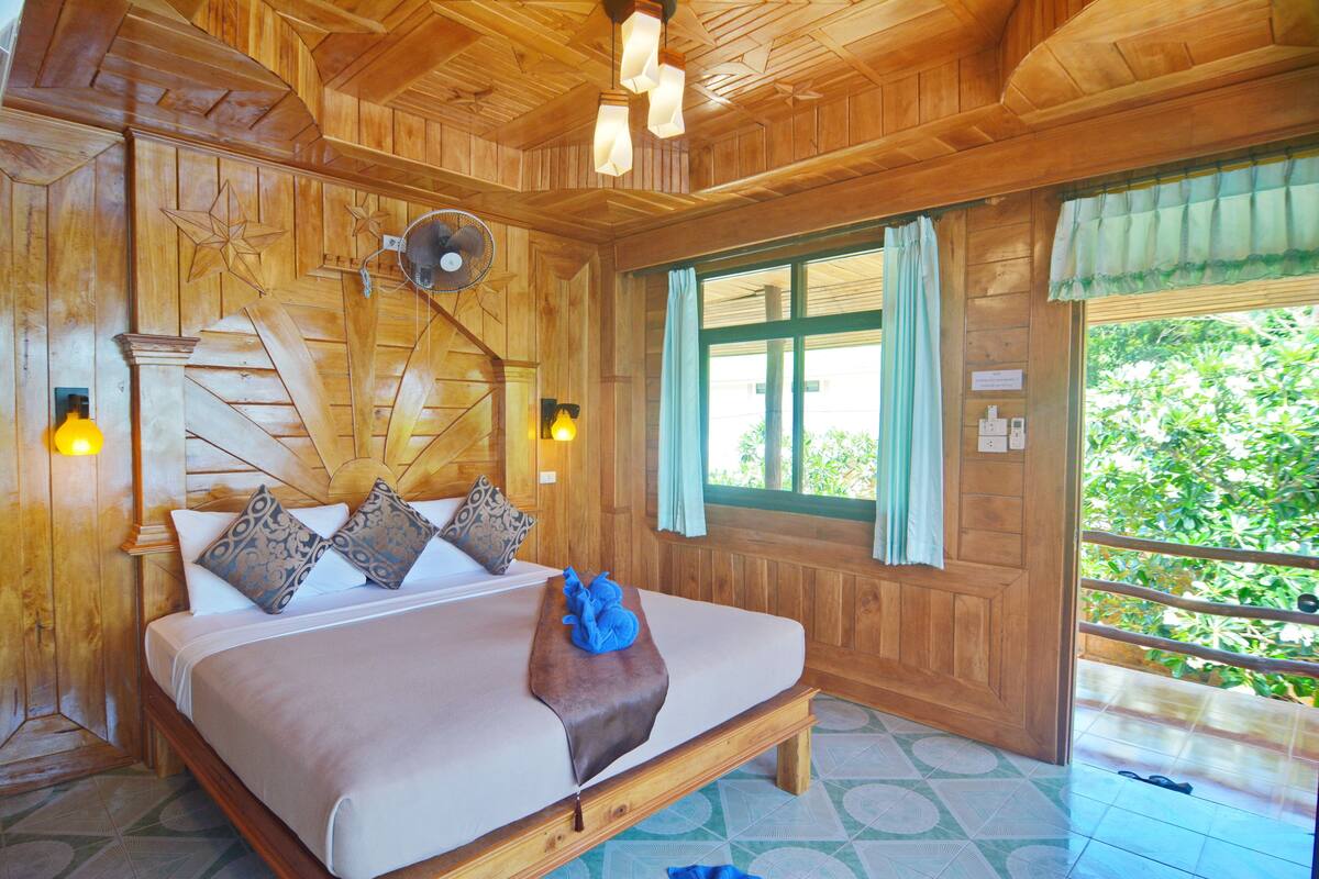 A wooden room with a bed, a fan, and a window with curtains.