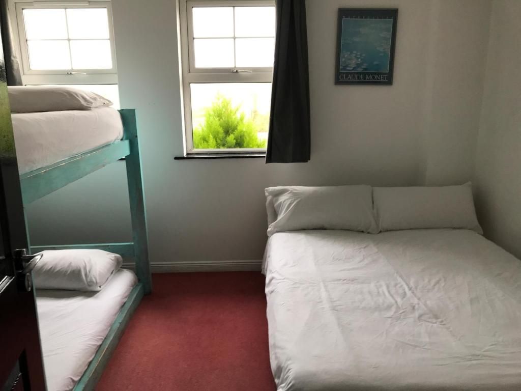 A room with bunk beds and a single bed, a window with curtains, and a wall-mounted picture.