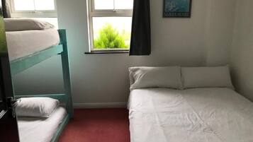 A room with bunk beds and a single bed, a window with curtains, and a wall-mounted picture.