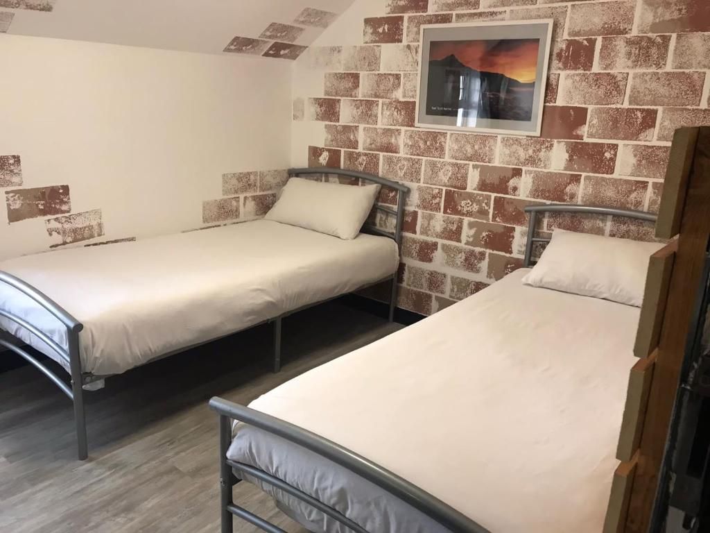 A room with two single beds, a brick wall, and a framed picture.