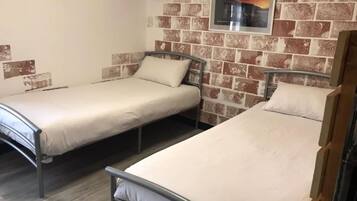 A room with two single beds, a brick wall, and a framed picture.