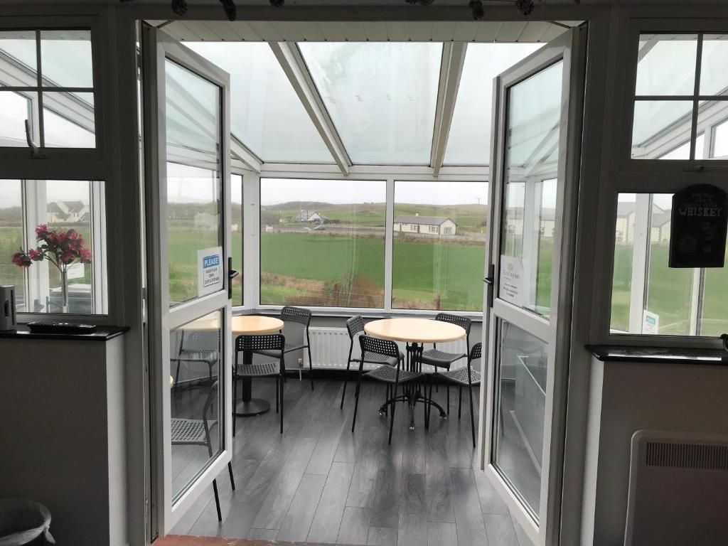 A conservatory with a view of a green field, a table with chairs, and a sign indicating a whiskey brand.