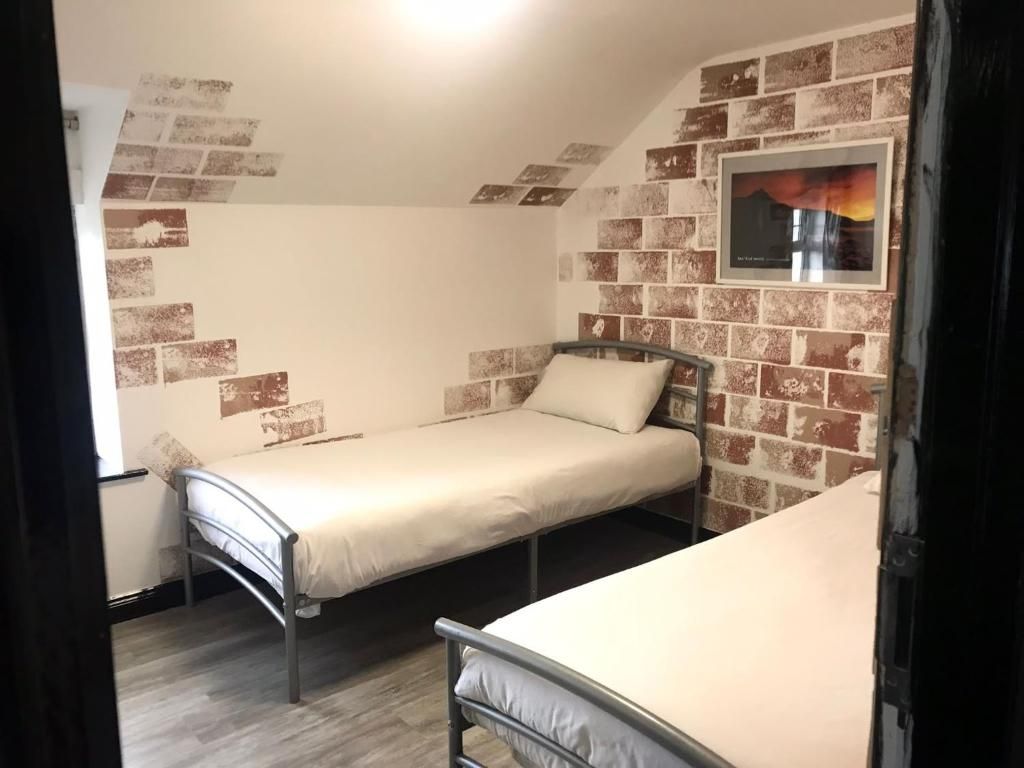 Una habitación con dos literas metálicas, una pared con estampado de ladrillo y un cuadro enmarcado.