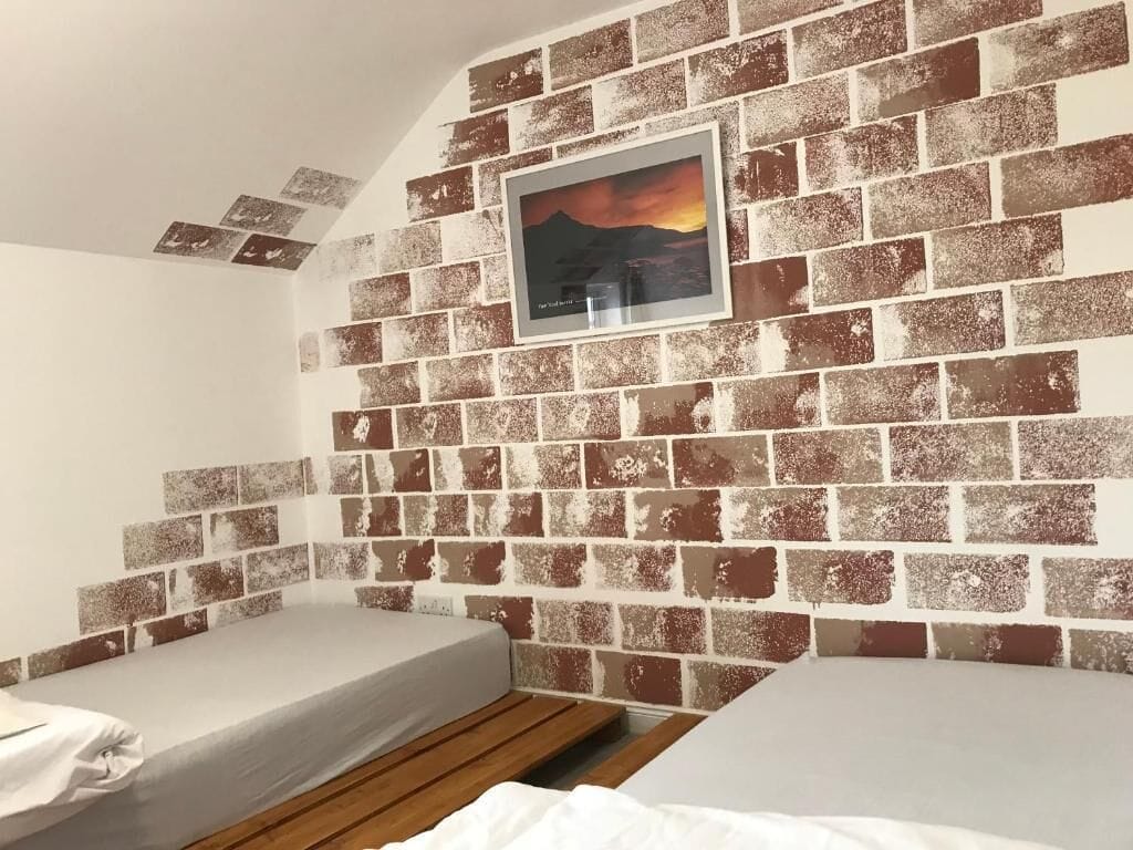 Una habitación con dos camas, una pared de ladrillo y un cuadro enmarcado.