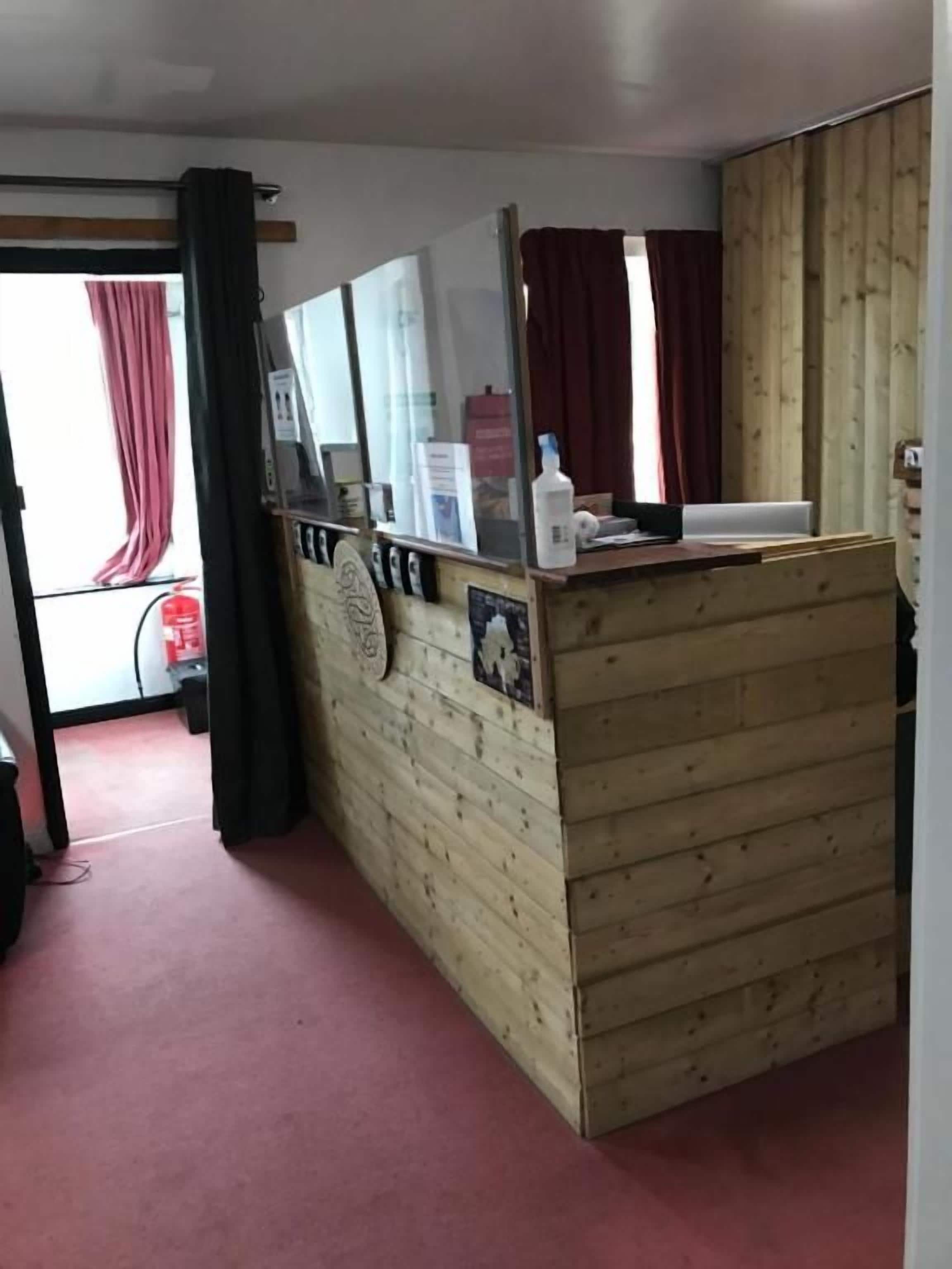 Une pièce avec un paravent en bois, un miroir, une petite table sur laquelle se trouve une bouteille, et un rideau rouge.