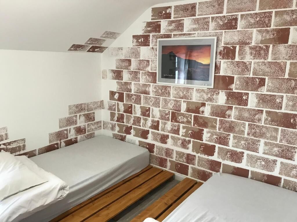 A small room with two beds, a brick-patterned wall, and a framed picture.