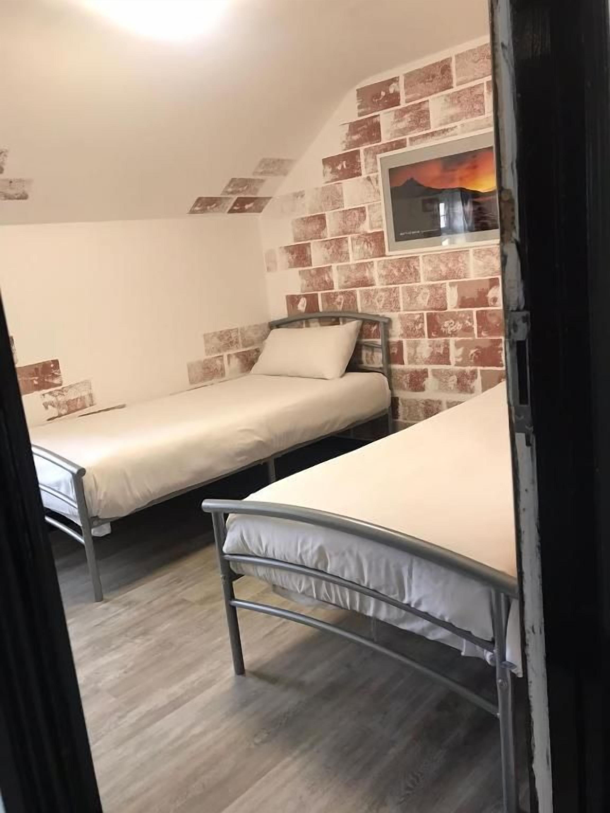 Una habitación con dos literas metálicas, una pared de ladrillo y un estante pequeño con una fotografía.