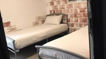 Una habitación con dos literas metálicas, una pared de ladrillo y un estante pequeño con una fotografía.