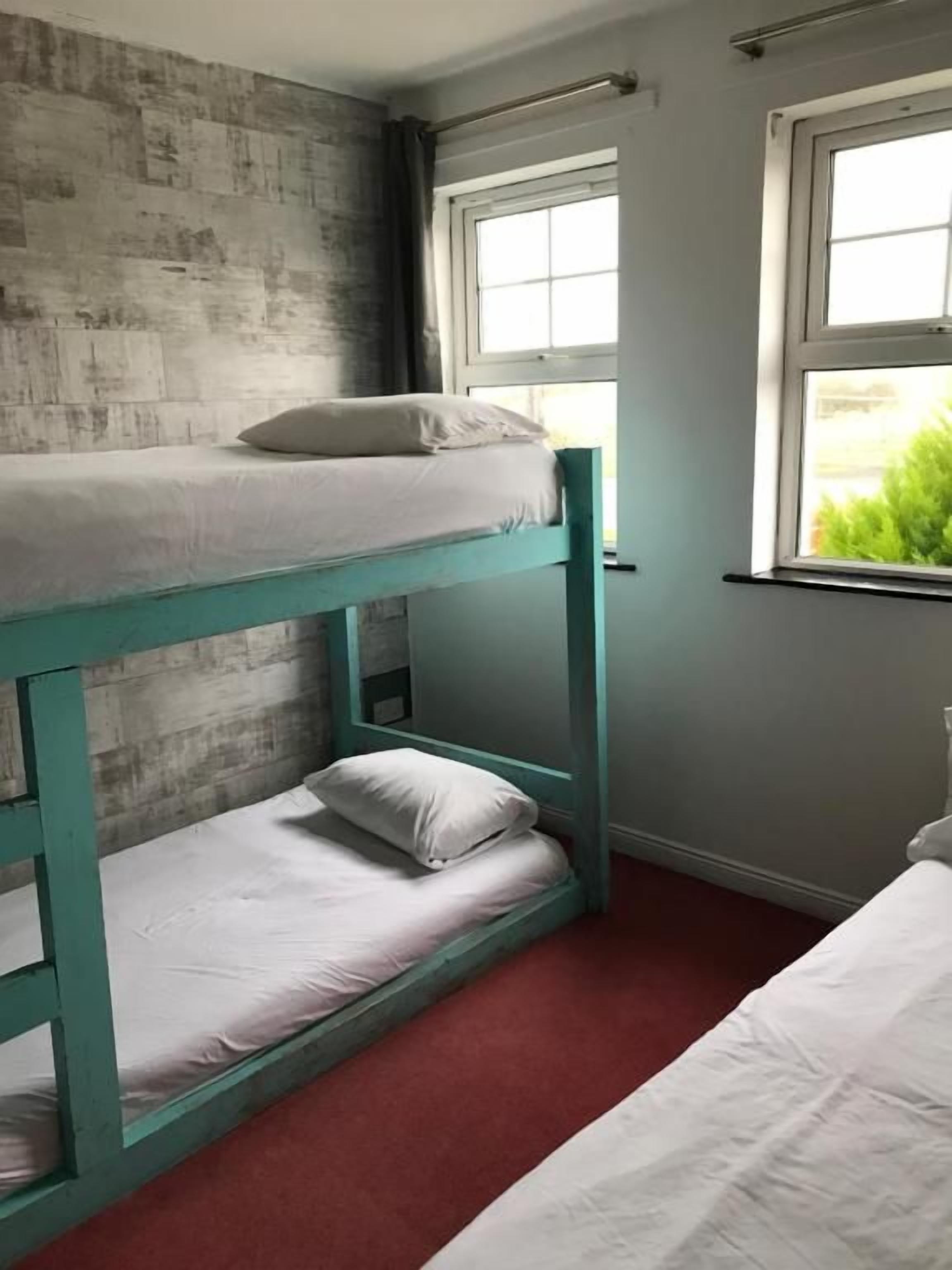 A bunk bed with a teal frame in a room with a red carpet and a window with curtains.