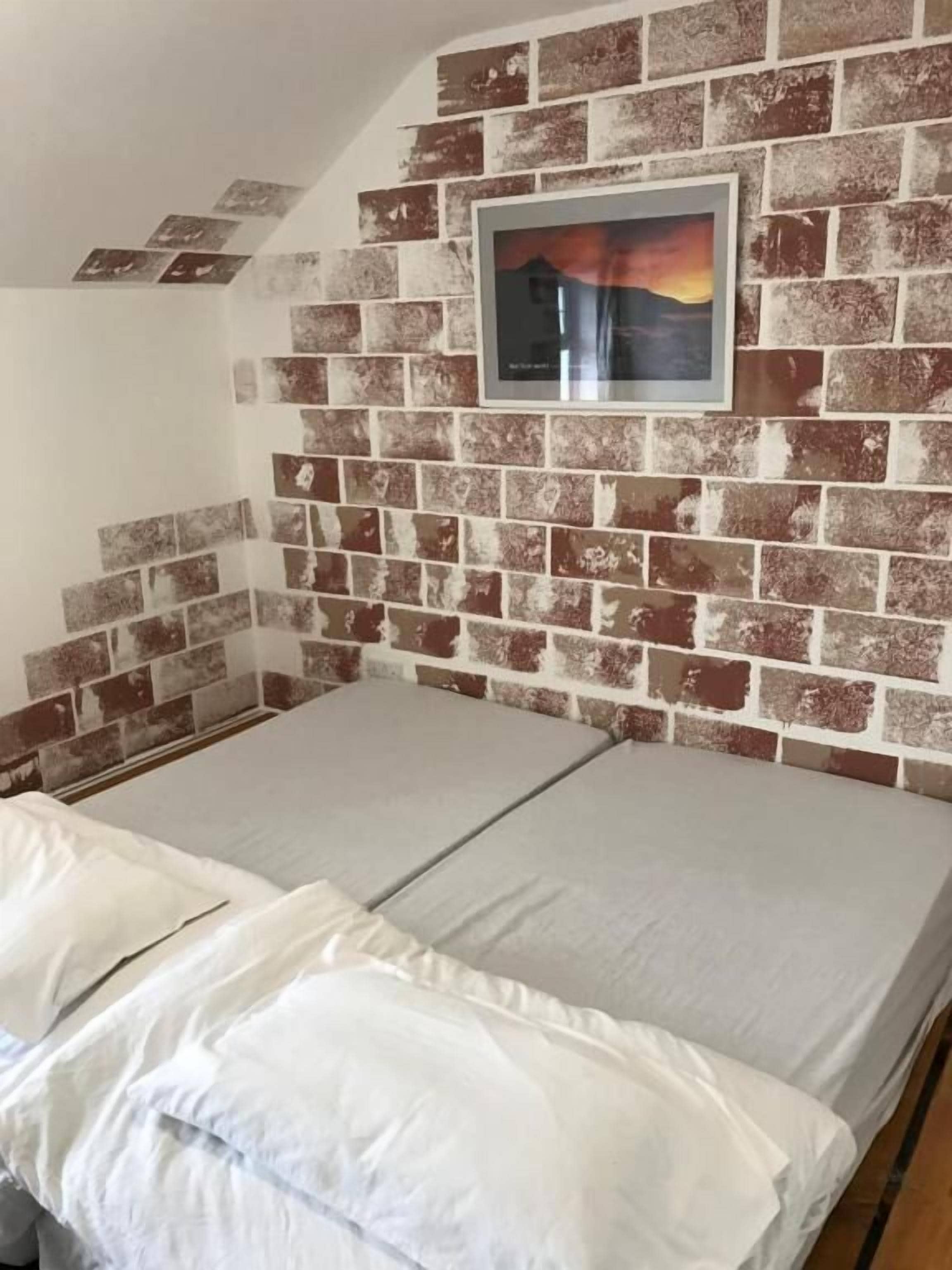 Una stanza con parete a mattoni, un quadro incorniciato e un letto con biancheria bianca.