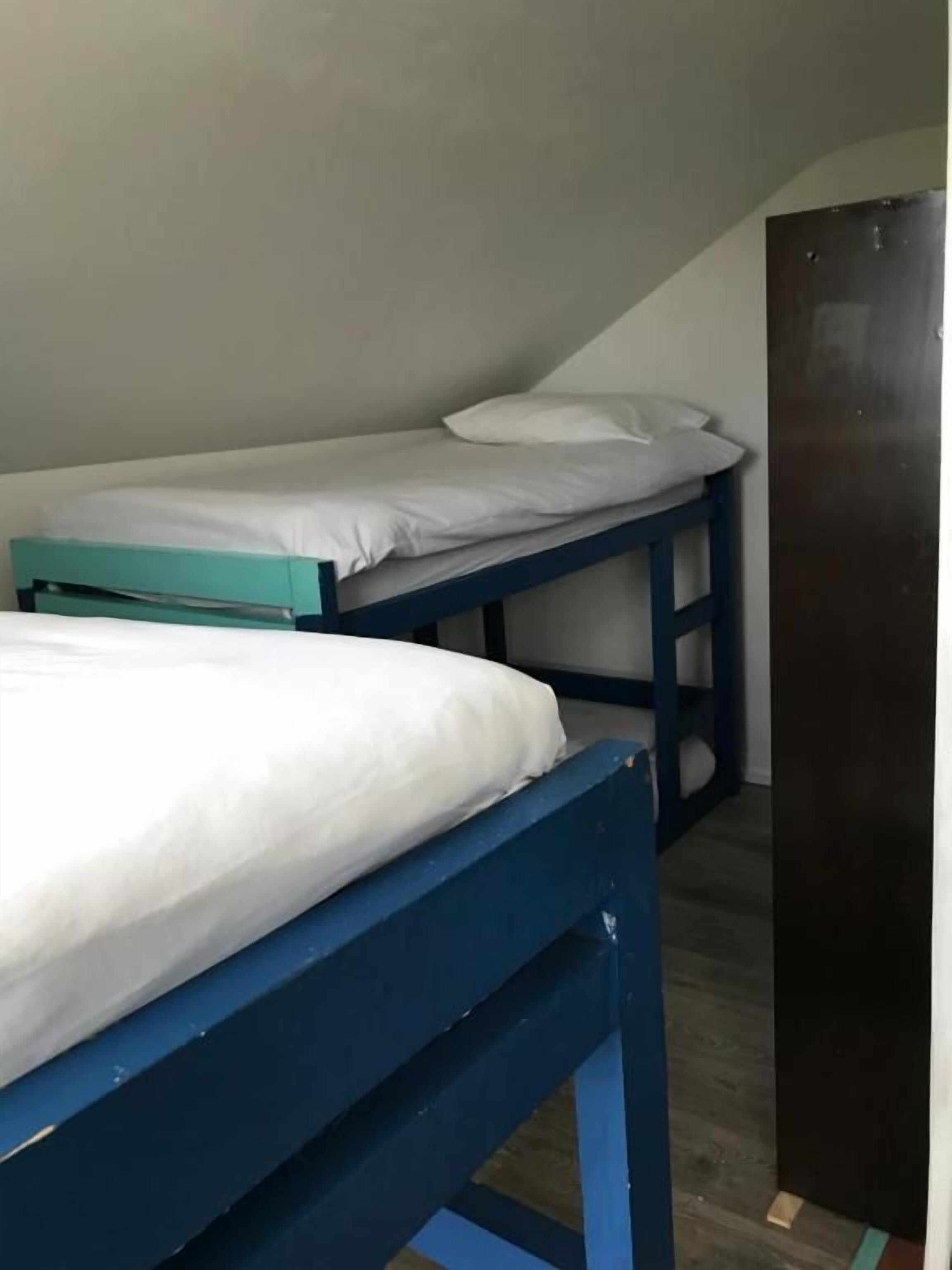 Una habitación con dos literas, una con estructura azul y otra con estructura verde azulado, y una puerta de madera.