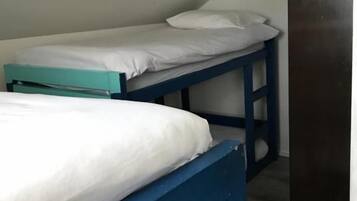 Una habitación con dos literas, una con estructura azul y otra con estructura verde azulado, y una puerta de madera.