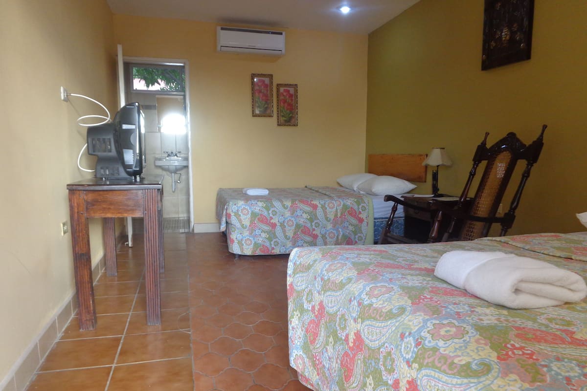 A hotel room with two beds, a desk, a chair, a sink, and an air conditioner.