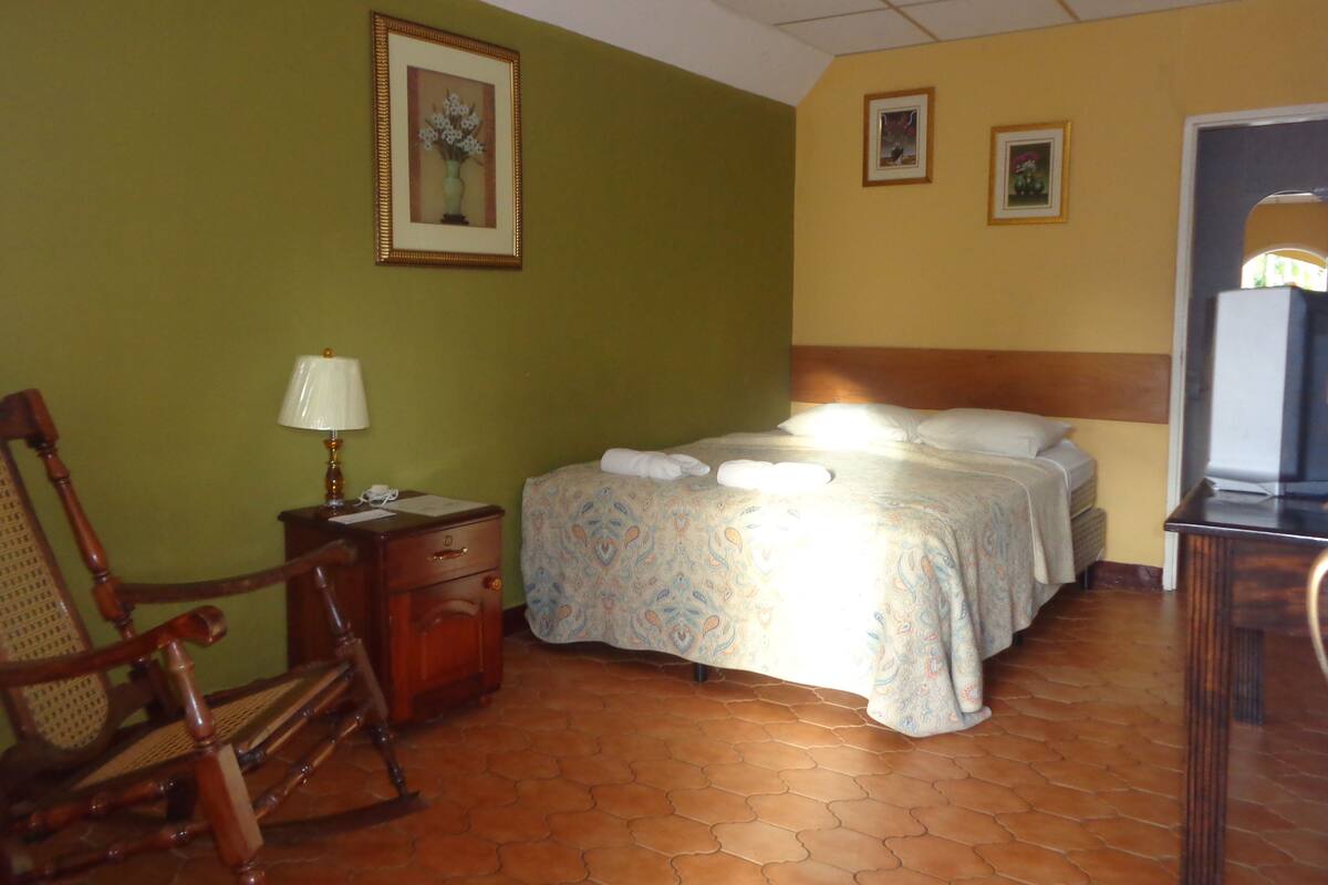 A hotel room with a bed, a chair, a nightstand, and a television.