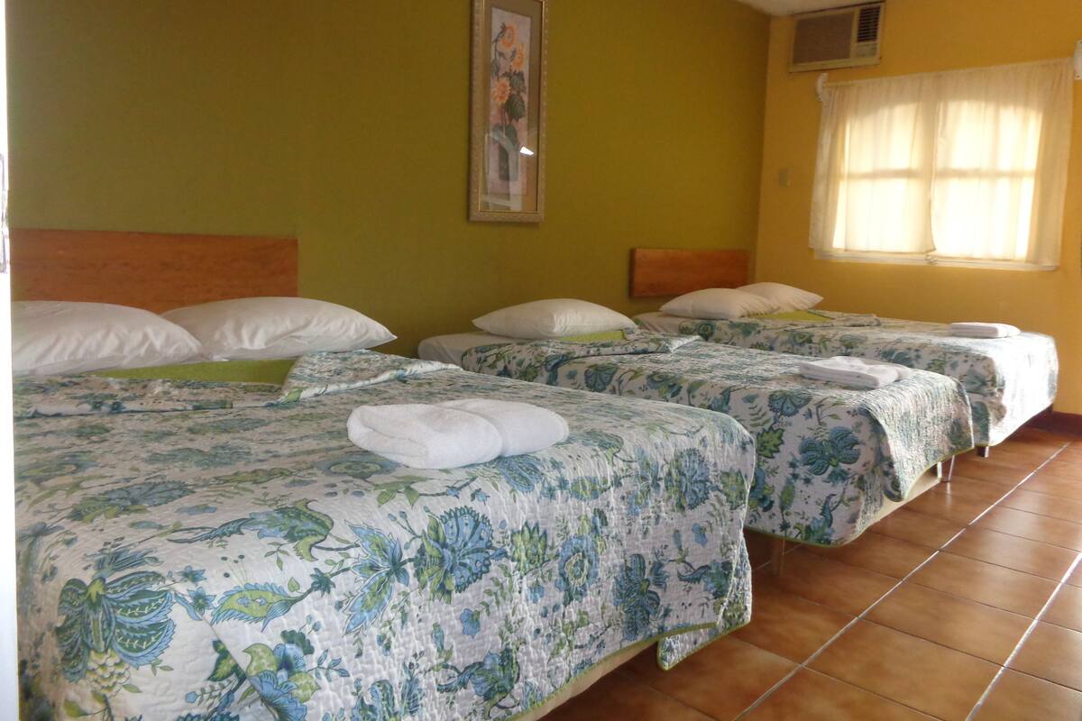 A hotel room with three beds, each with floral-patterned bedding and white pillows.