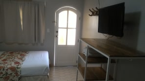 A room with a bed, a wooden TV stand, a door with a window, and a tiled floor.