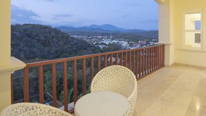 A balcony with wicker furniture and a view of a town and mountains.