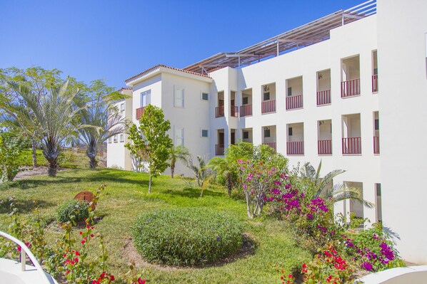 A white building with multiple balconies and a garden with various plants and flowers. - Mansiones Cruz del Mar Huatulco (Santa María Huatulco)
