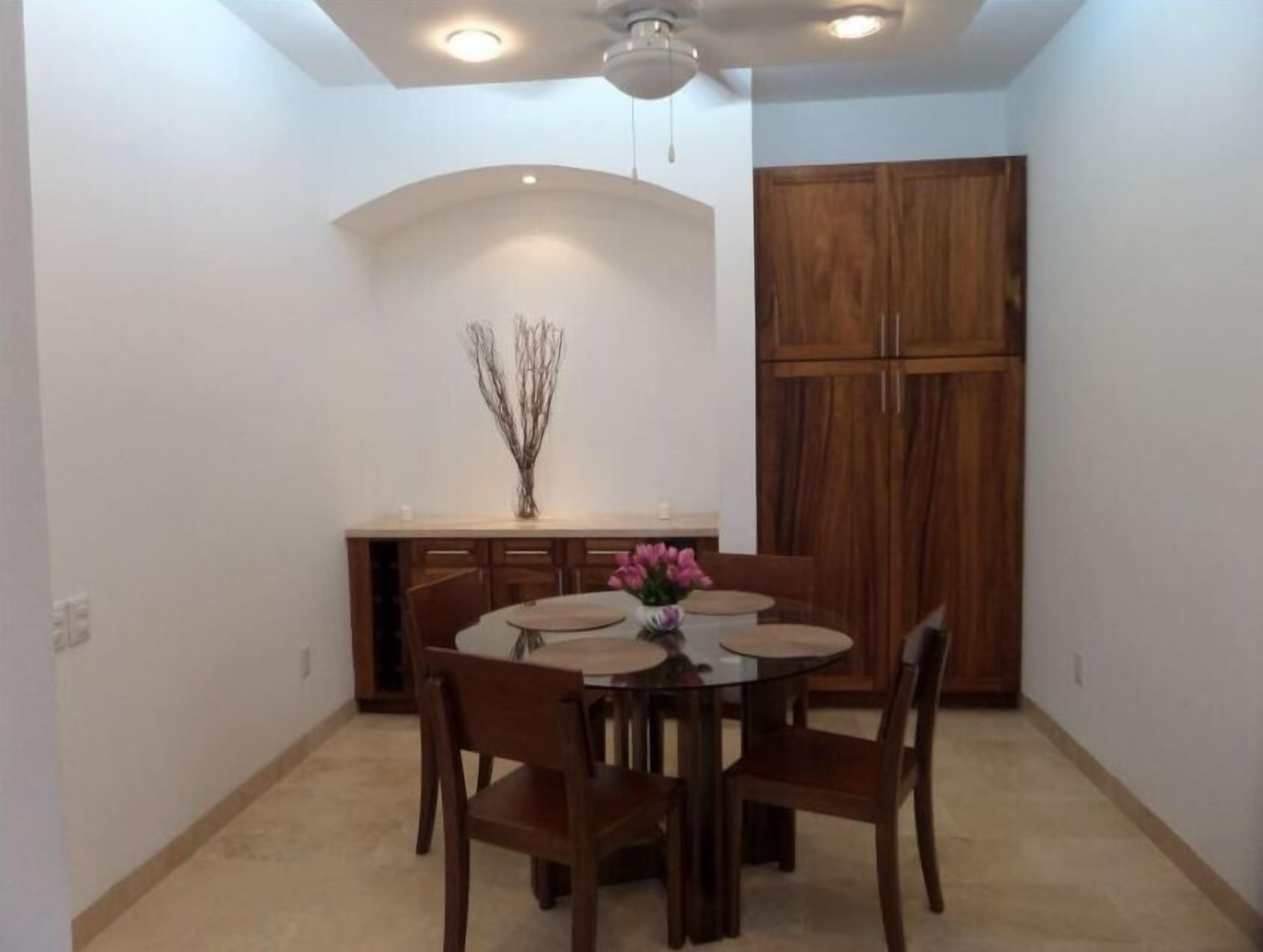 Un comedor con una mesa redonda, seis sillas, un florero con flores y un armario de madera.