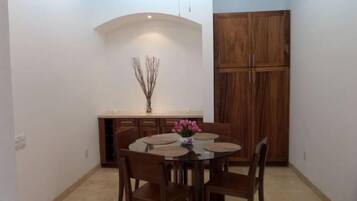 Un comedor con una mesa redonda, seis sillas, un florero con flores y un armario de madera.