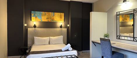 A modern hotel room with a bed, bedside tables, a desk, and a large mirror.