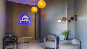 Een hotel lobby met een modern design, met een receptiebalie, een zithoek en een neonbord met de naam van het hotel.