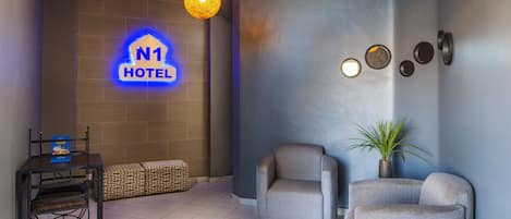Un vestíbulo de hotel con diseño moderno, que incluye un mostrador de recepción, zona de estar y un letrero de neón con el nombre del hotel.