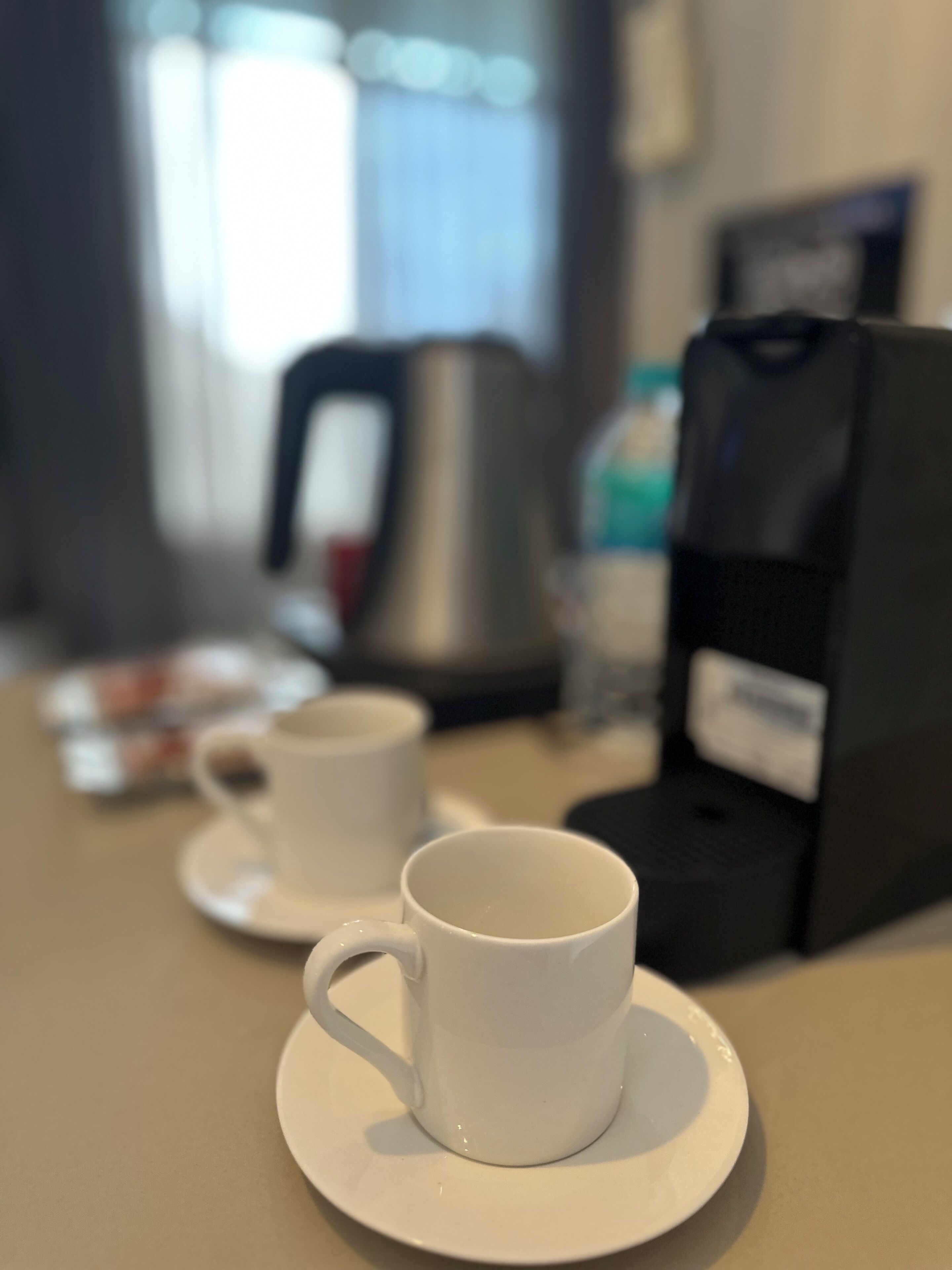 Una estación de café con dos tazas blancas sobre platillos, una cafetera y un paquete de café.