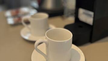 Una estación de café con dos tazas blancas sobre platillos, una cafetera y un paquete de café.