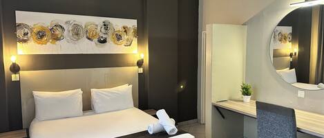 Una habitación de hotel con una cama grande, lámparas de noche, un escritorio con una silla, un espejo y una obra de arte en la pared.