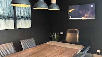 Un espace de salle à manger moderne avec une table en bois, des murs noirs et deux lampes suspendues.