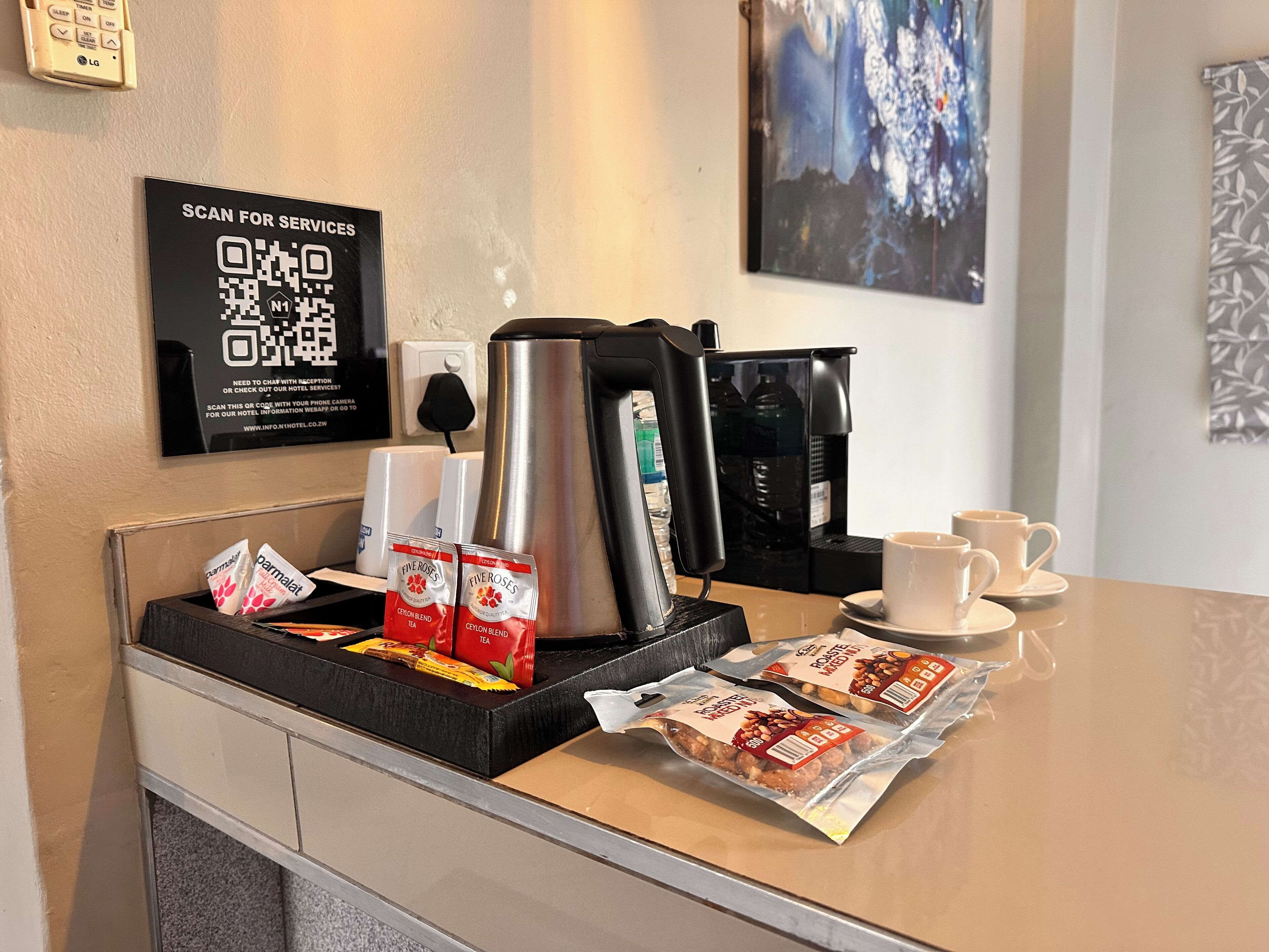 Un espace d’accueil d’hôtel comprenant un coin café, des sachets de thé, une bouilloire et un code QR encadré donnant accès aux services proposés.