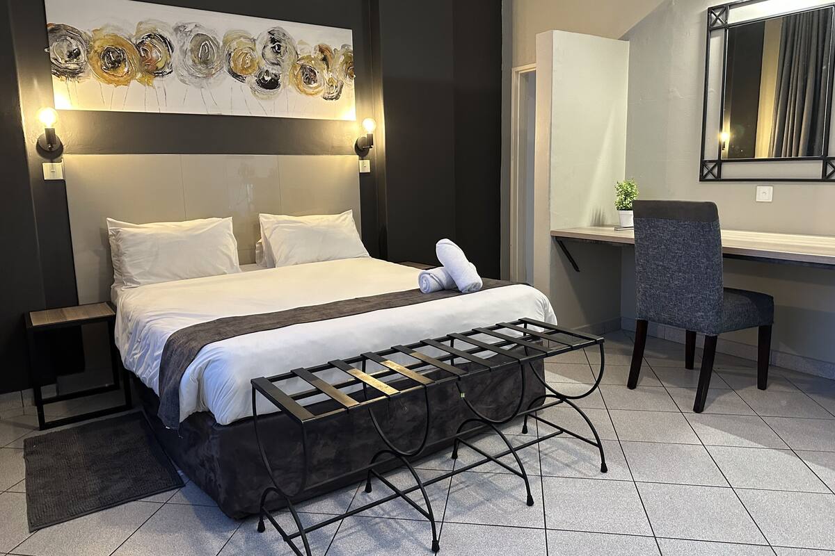 Een moderne slaapkamer met een groot bed, een nachtkastje, een stoel, een bureau en een kunstwerk aan de muur.