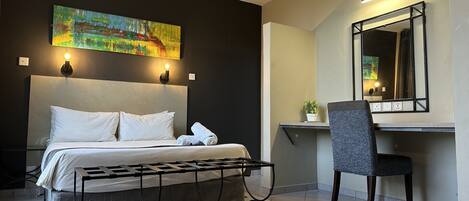 A modern hotel room with a bed, a desk, a chair, and a painting on the wall.