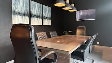 A modern conference room with a wooden table, black leather chairs, and three pendant lights.