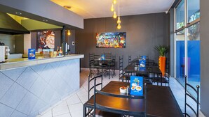 Een modern restaurant in een hotel, met een balie, eettafels, stoelen en een groot schilderij aan de muur.