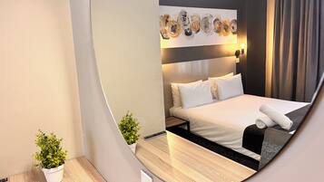 A modern hotel room with a large bed, a bedside table, a small potted plant, and a wall-mounted artwork.