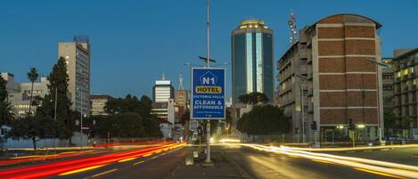 A city street at dusk with a hotel sign indicating 'N1 HOTEL VICTORIA FALLS CLEAN & AFFORDABLE'.