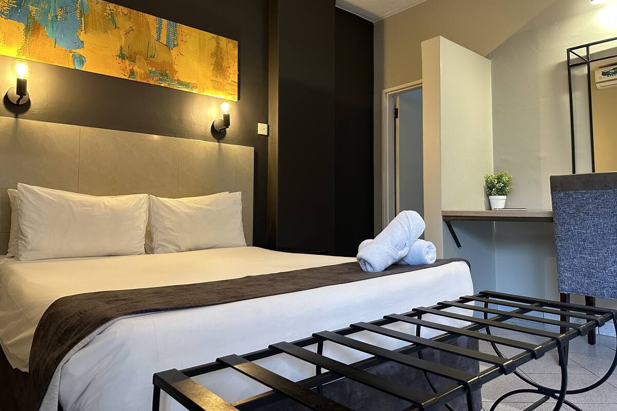 Een hotelkamer met een bed, hoofdbord, een wandlamp, handdoek, een kleine plant en een stoel.