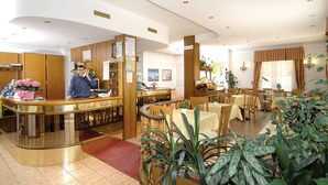 A hotel lobby with a reception desk, dining area, and a large potted plant. - Hotel Savoia (Ospedaletti)