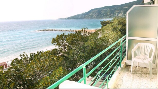 A balcony with a white plastic chair, overlooking a beach and ocean. - Hotel Savoia (Ospedaletti)