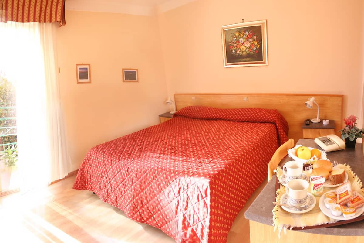 Een hotelkamer met een bed, nachtkastje met lamp, telefoon en een ontbijttafel.