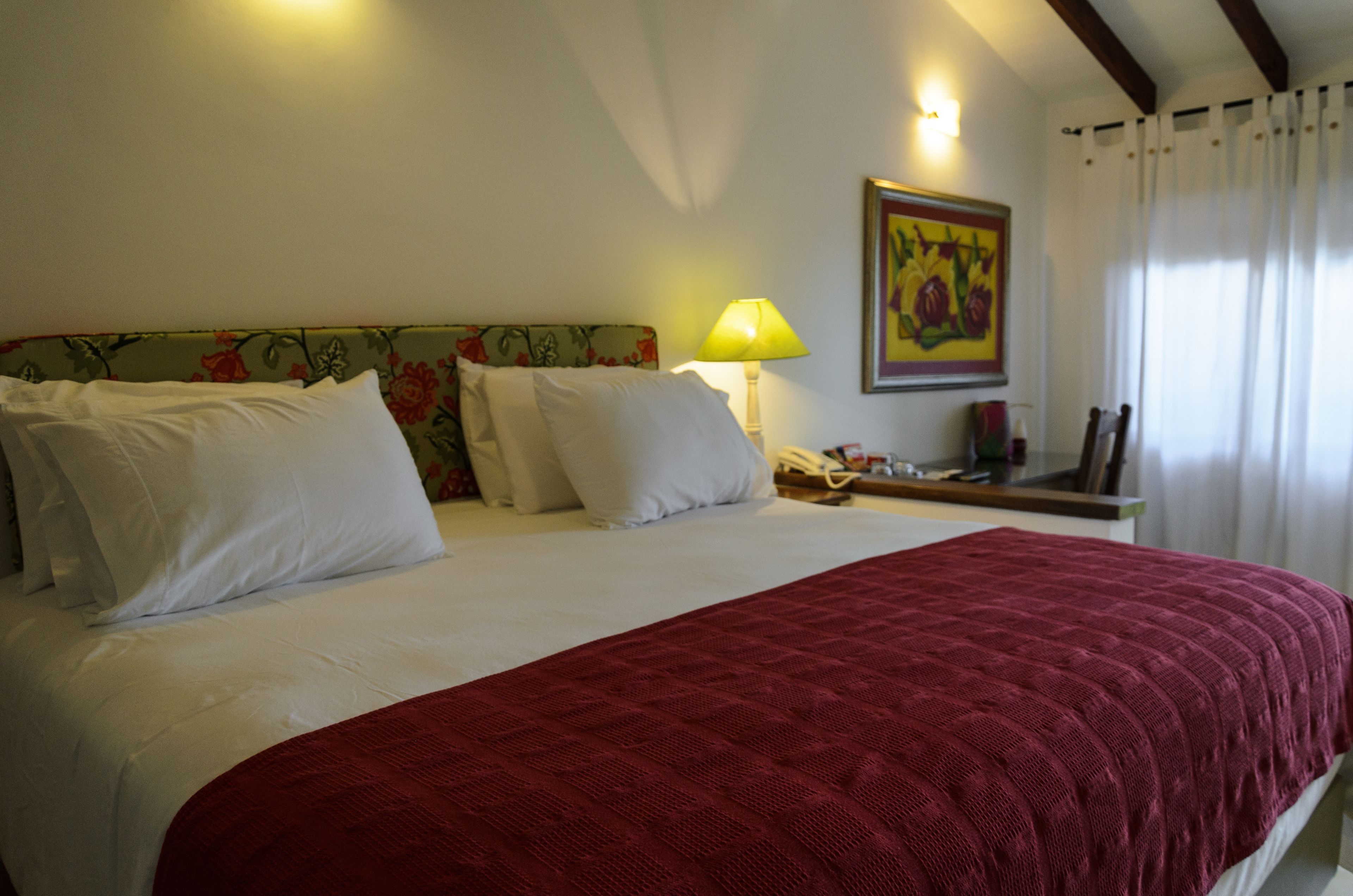 A hotel room with a large bed, a floral headboard, a bedside lamp, and a painting on the wall.