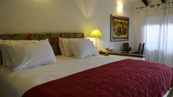 A hotel room with a large bed, a floral headboard, a bedside lamp, and a painting on the wall.