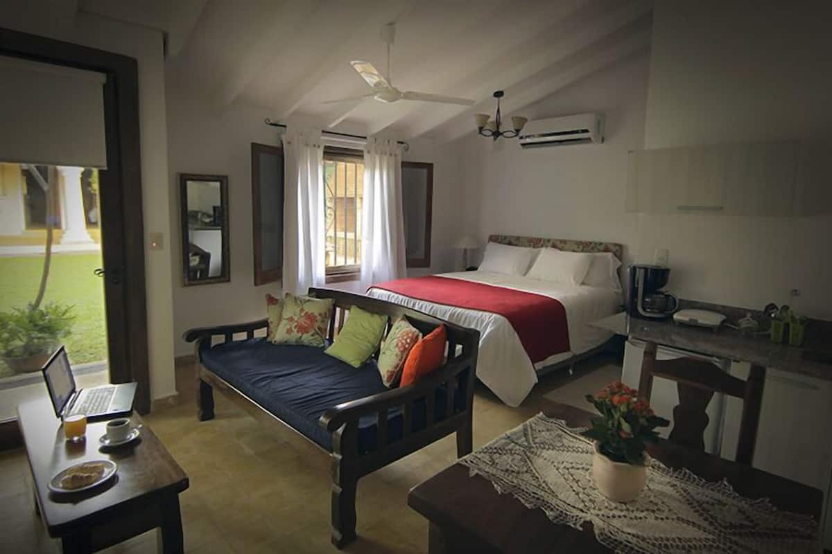 A bedroom with a bed, a desk, a laptop, and a coffee maker.