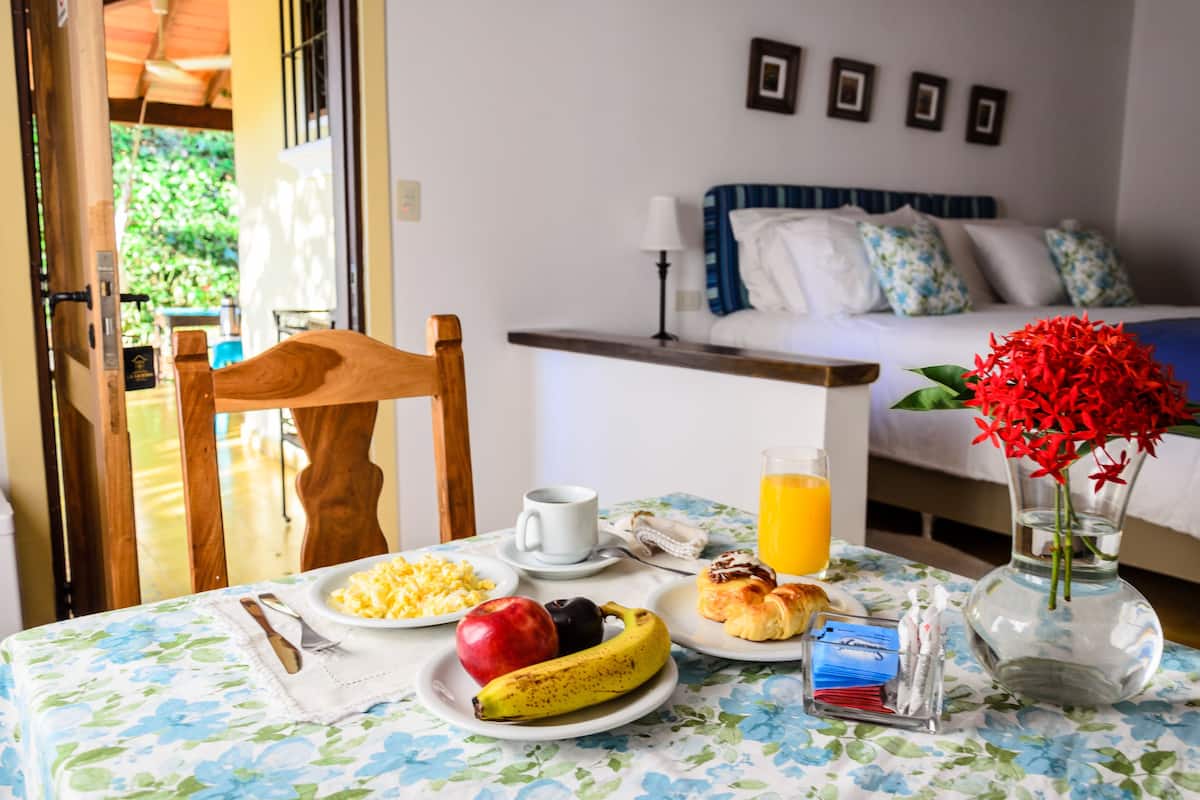A breakfast table with plates of food, a cup, a banana, and a vase with flowers.