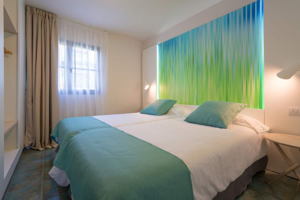 A bedroom with a large bed, two pillows, a bedside table, and a window with curtains.