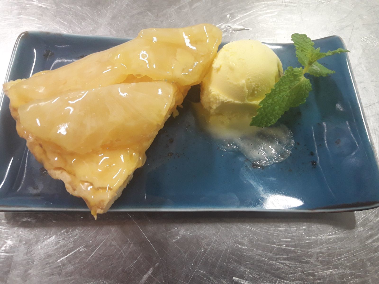 Un piatto dessert con una fetta di torta rovesciata all'ananas e una pallina di gelato alla vaniglia, guarnito con una fogliolina di menta.